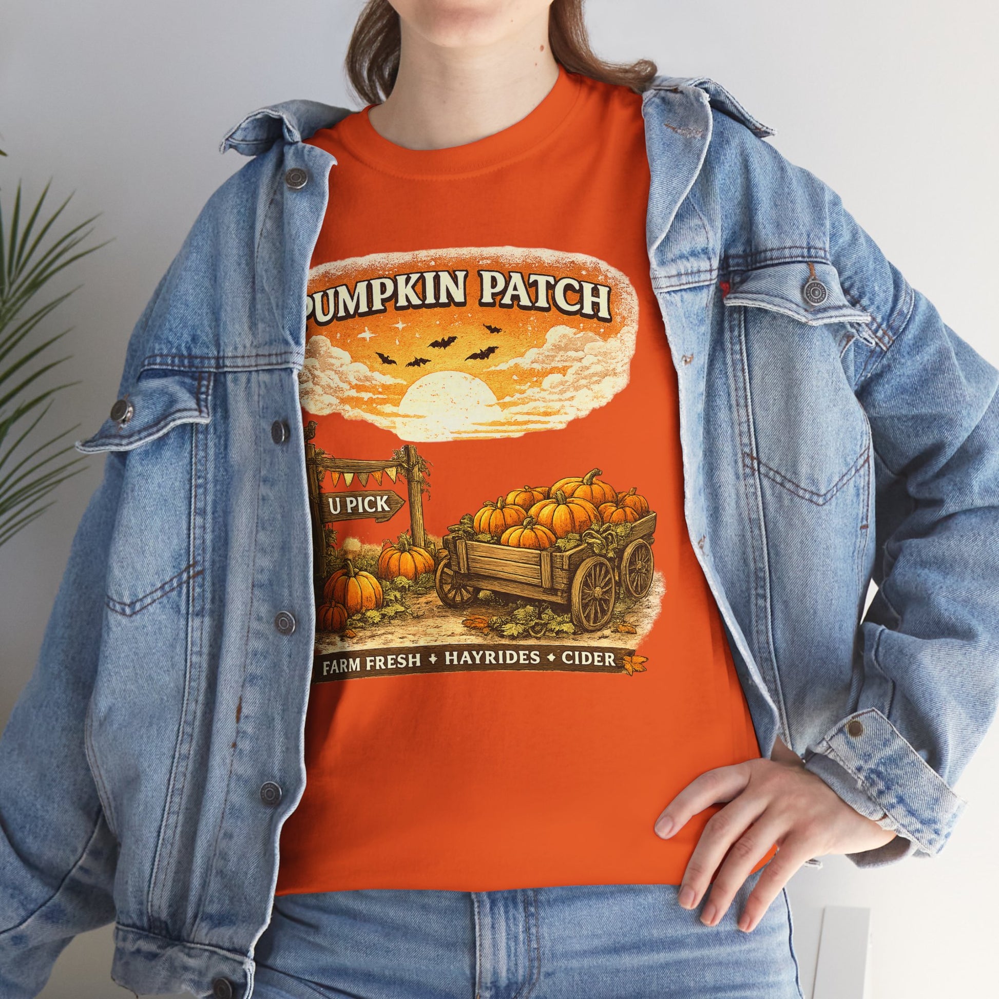 A person wearing an orange graphic T-shirt with a vintage-style pumpkin patch print, layered under a light blue denim jacket.