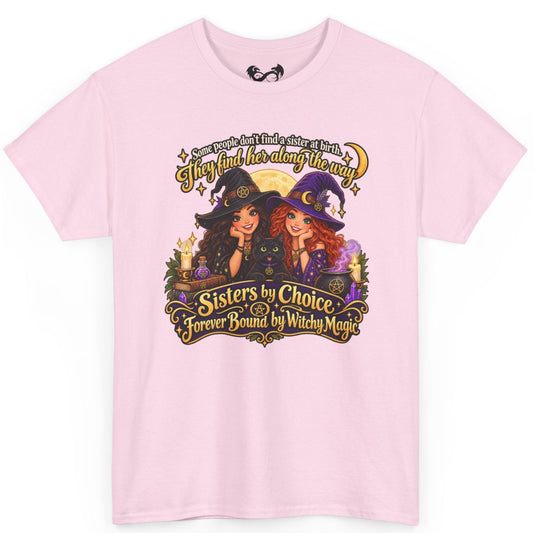 A light pink short-sleeve crewneck t-shirt featuring a colorful graphic print of two cartoon witch sisters with the text 'Sisters by Choice Forever Bound by Witch Magic' on a plain white background.