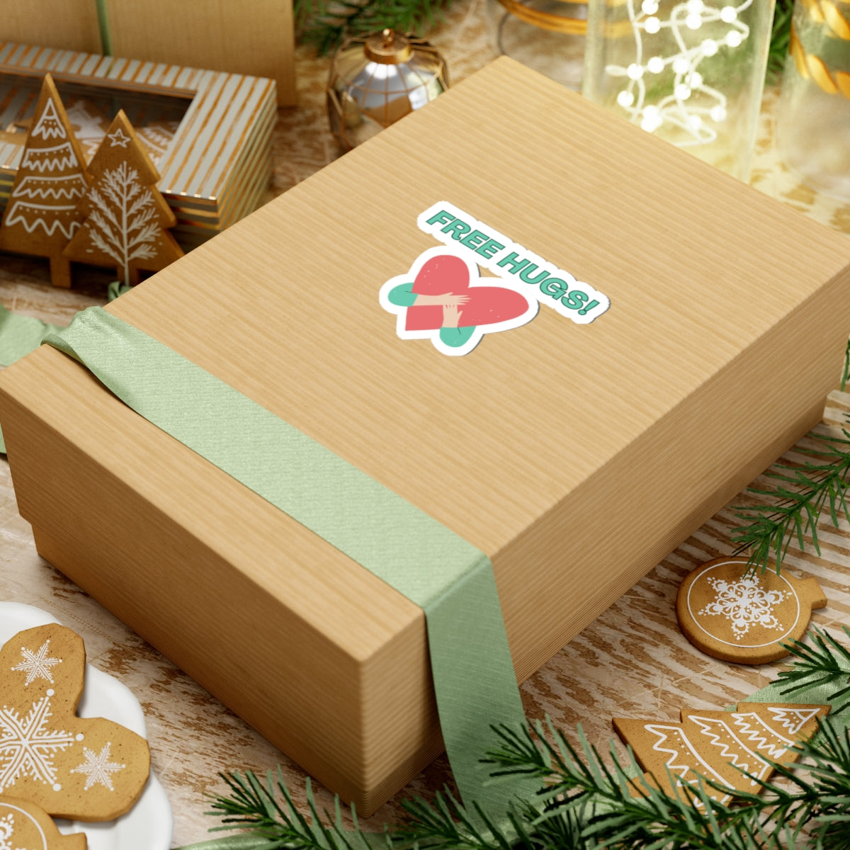 Gift box with a green ribbon and 'Free Hugs!' sticker on a festive background with cookies and decorations.