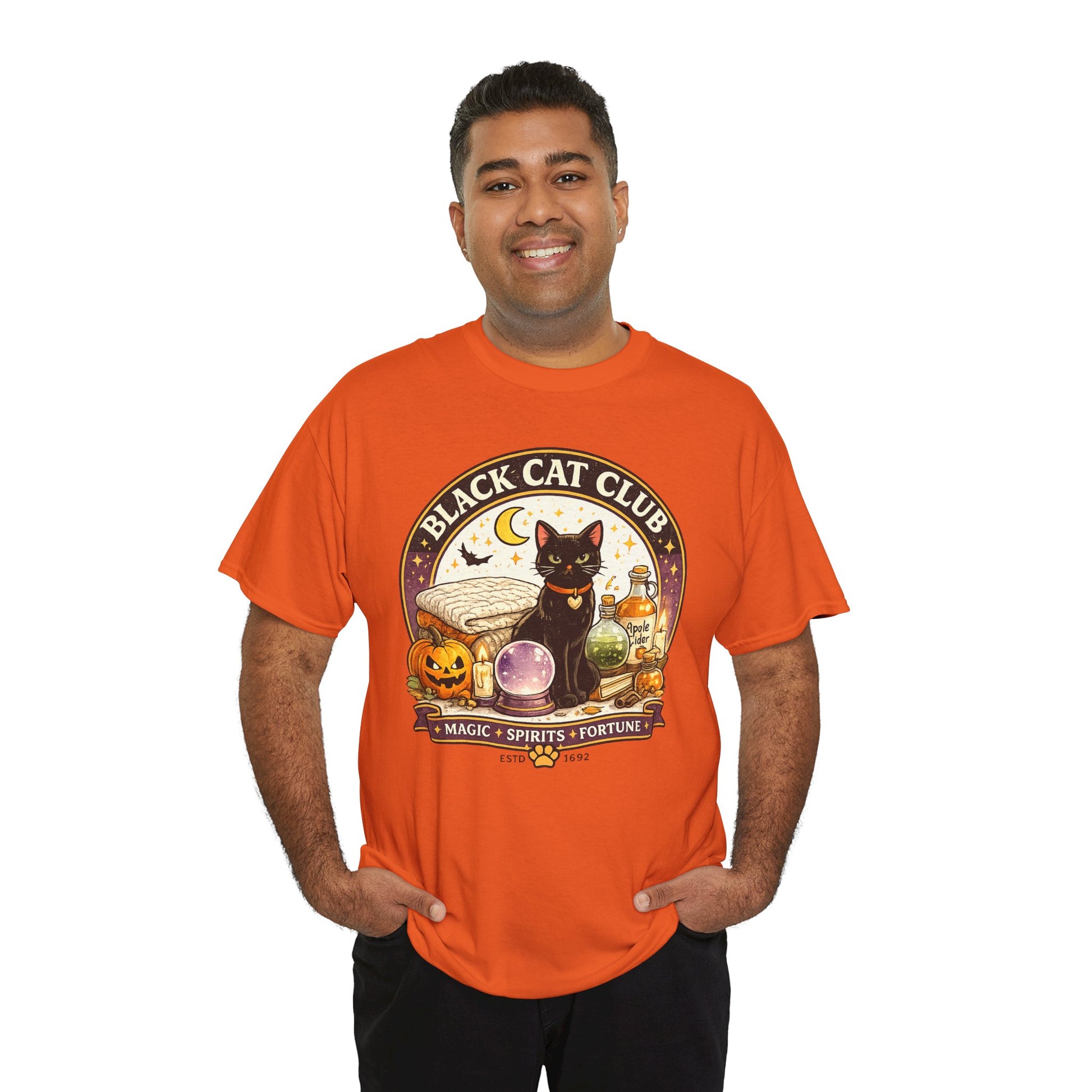 A man wearing a bright orange graphic t-shirt with a 'Black Cat Club' Halloween design featuring a black cat, a crystal ball, and pumpkins, set against a plain white background.