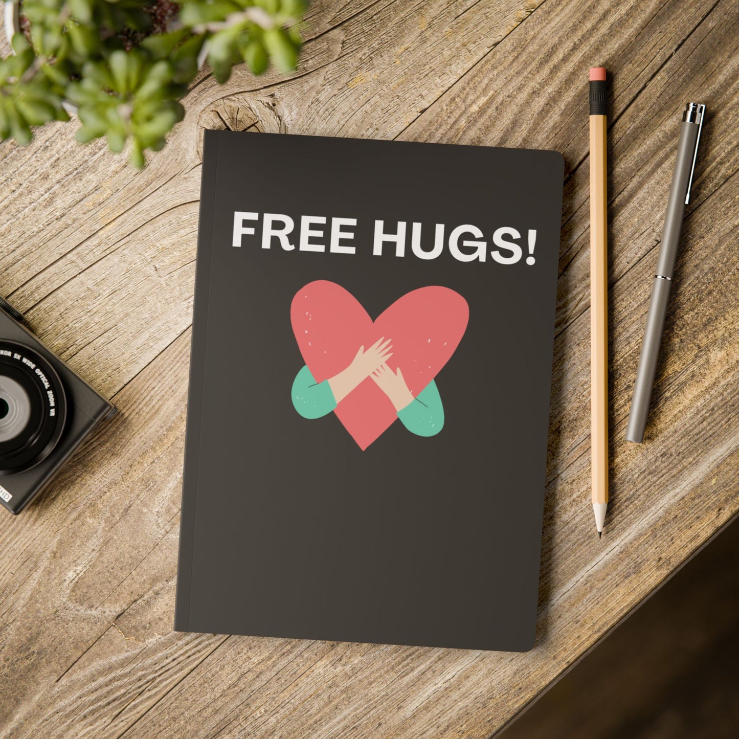 Notebook with 'FREE HUGS!' design on a wooden surface with a pencil and pen.