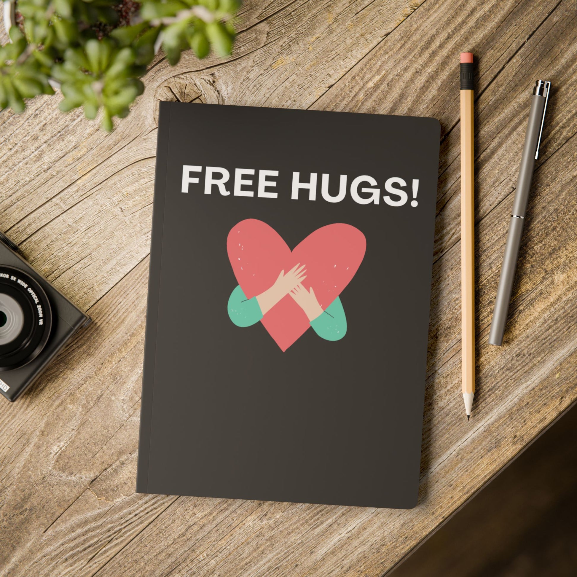 Notebook with 'FREE HUGS!' design on a wooden surface with a pencil and pen.
