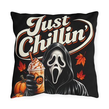 A square black throw pillow featuring a Halloween-themed graphic print with the text 'Just Chillin'', a Ghostface-style hooded figure holding an iced coffee, pumpkins, and orange autumn leaves.