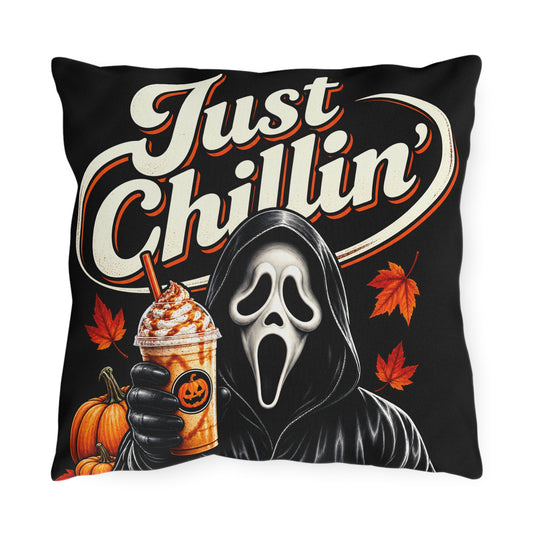 A square black throw pillow featuring a Halloween-themed graphic print with the text 'Just Chillin'', a Ghostface-style hooded figure holding an iced coffee, pumpkins, and orange autumn leaves.