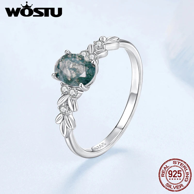Silver ring with a green gemstone on a light blue background, featuring the WOSTU brand.