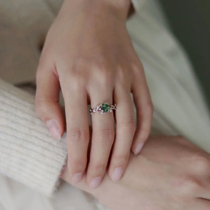 Close-up of a hand wearing a ring with a green gemstone on a neutral background
