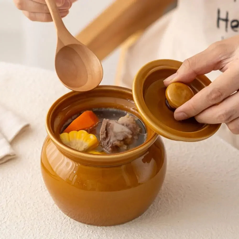 Brown ceramic pot with soup and a wooden spoon on a light background