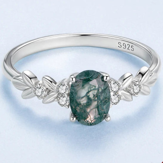 Silver ring with a green gemstone on a light blue background, featuring the WOSTU brand.