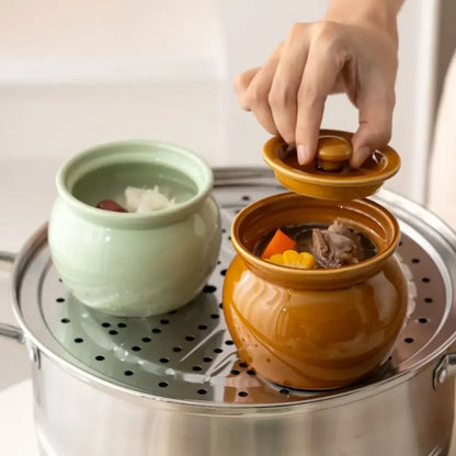 Two ceramic pots on a steamer with a hand lifting the lid of one pot.