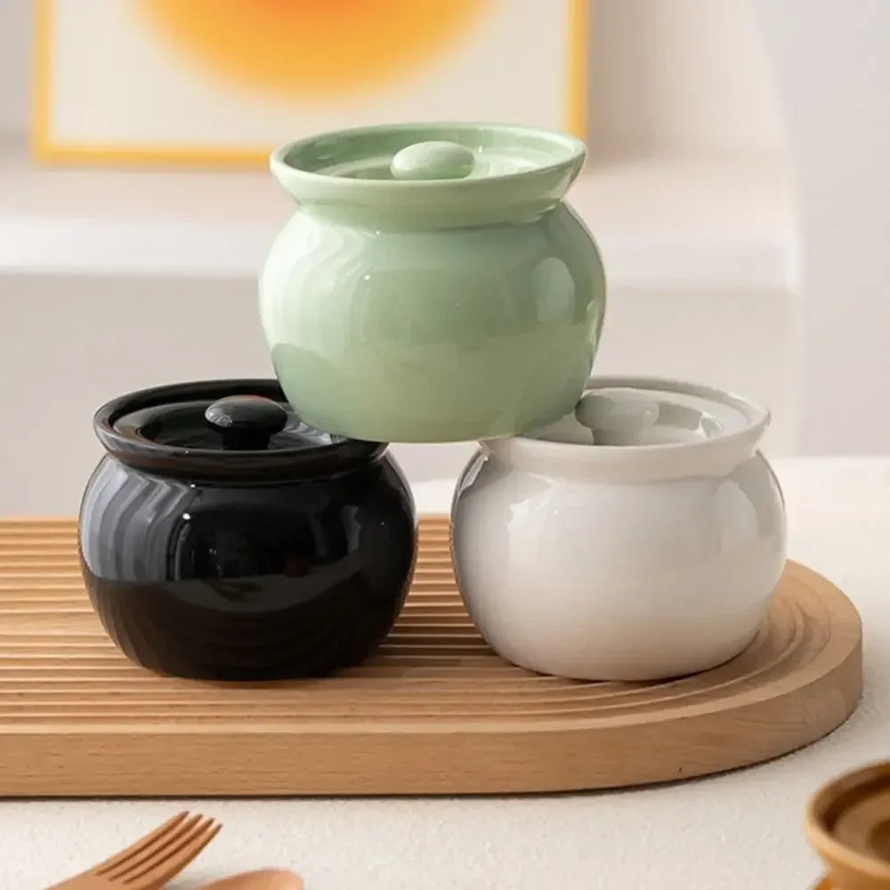 Three ceramic pots in black, green, and white on a wooden tray with a blurred background.