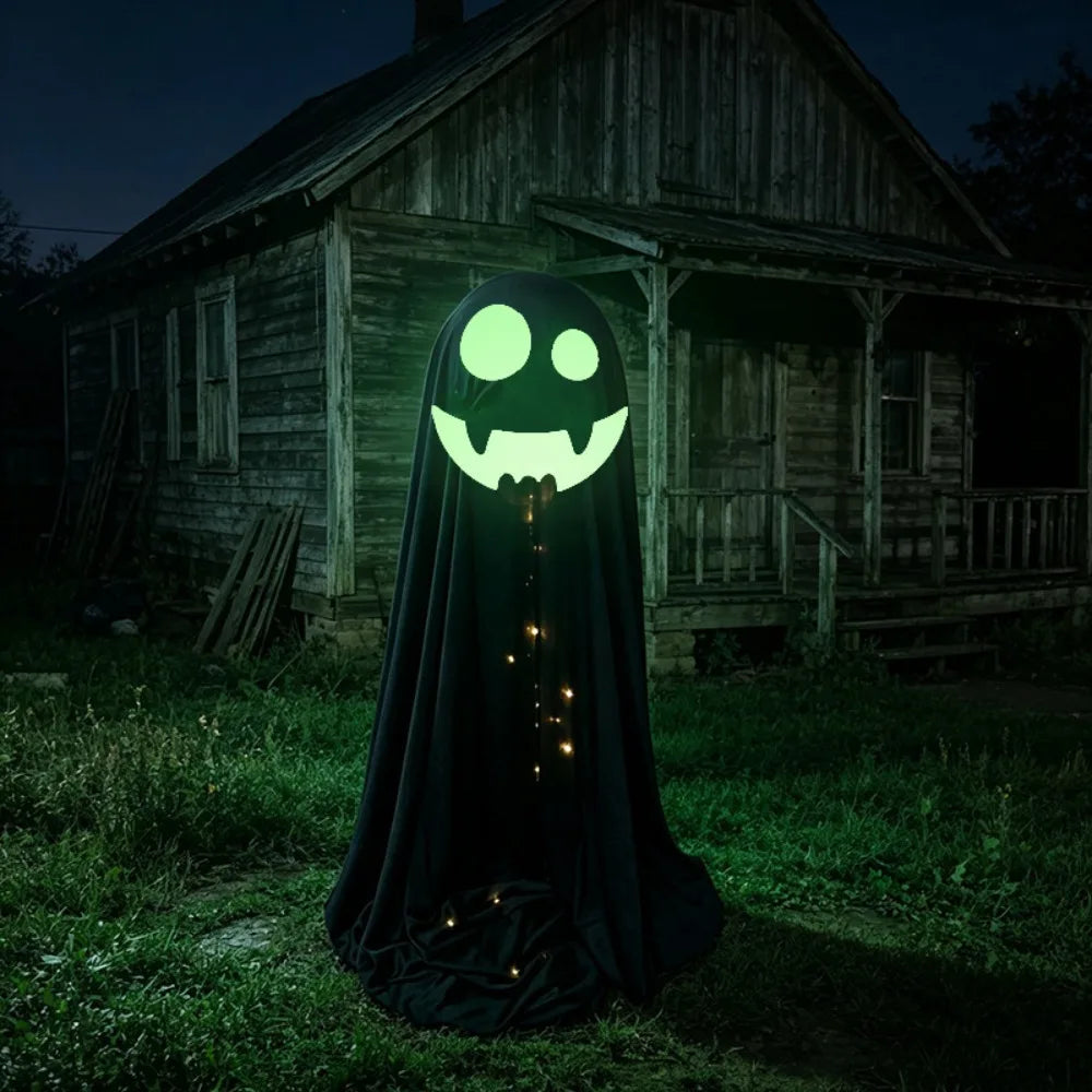 A Halloween ghost costume standing in a grassy yard at night in front of an old wooden house. The costume is black with a glowing green face and small warm lights hanging down the front.