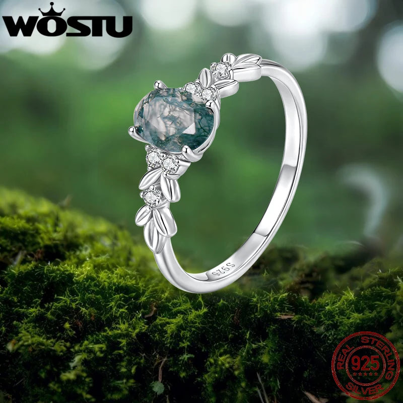Silver ring with a blue gemstone on a green moss background, featuring the WOSTU brand.