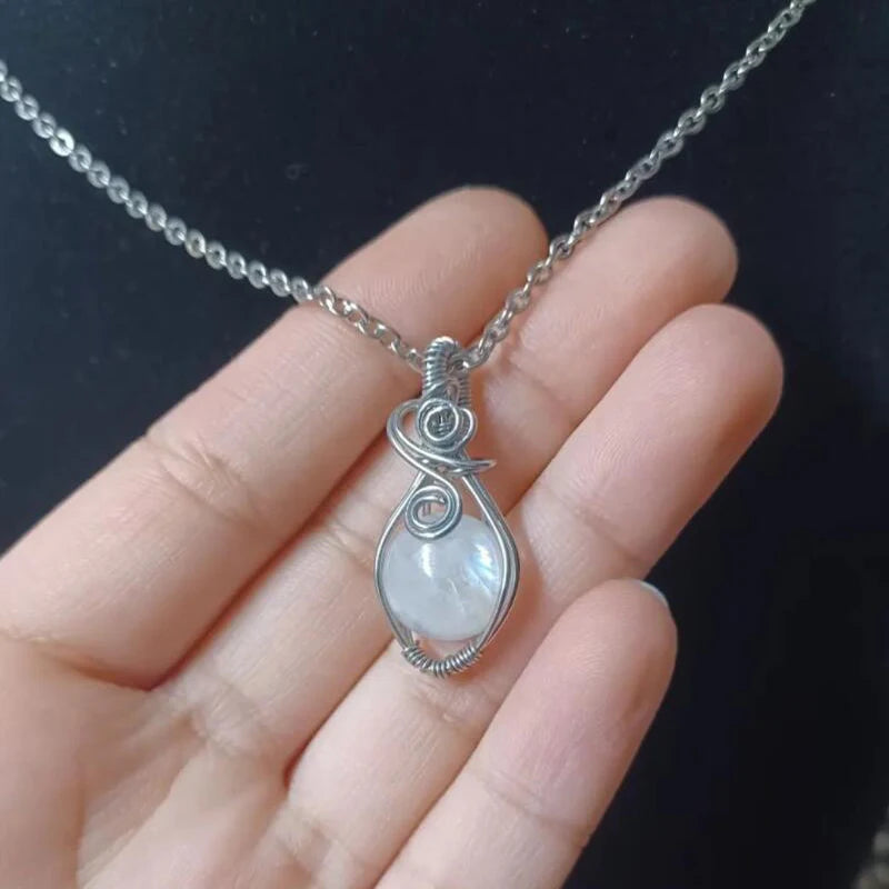 Silver necklace with a teardrop-shaped pendant held in a hand against a dark background
