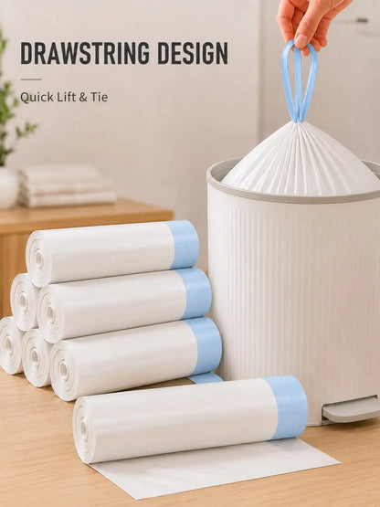 White trash bag rolls with light blue bands are shown on a wooden table beside a white trash can. A hand is lifting a bag by its blue handle, and the text 'DRAWSTRING DESIGN Quick Lift & Tie' appears in the upper left.