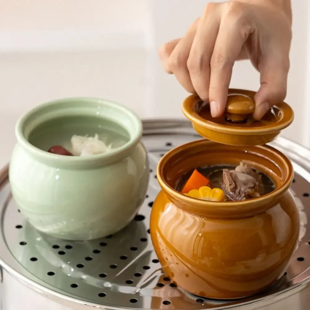 Two ceramic pots on a steamer with a hand opening one of them.