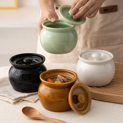 Four ceramic pots with lids in black, green, white, and brown on a light surface.
