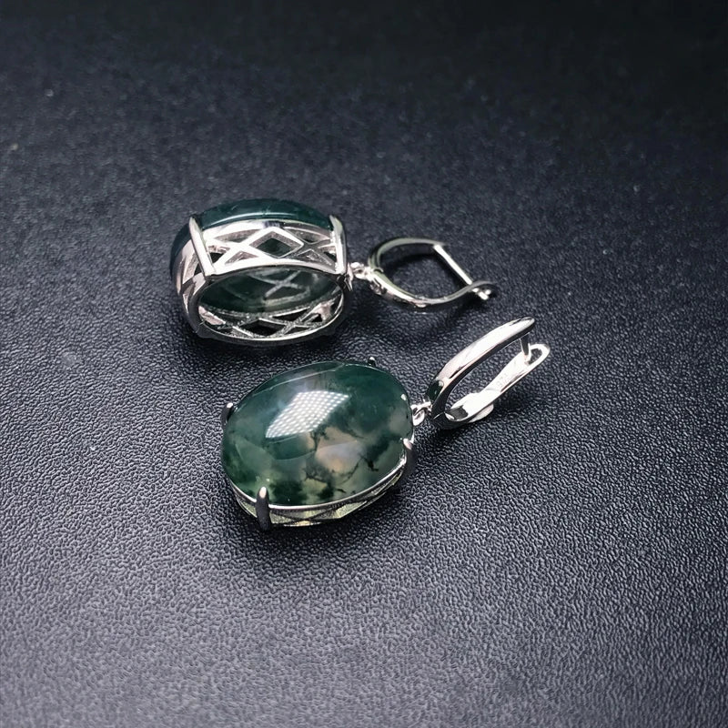 Two silver pendants with green gemstones on a dark surface
