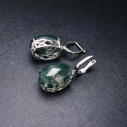 Two silver pendants with green gemstones on a dark surface