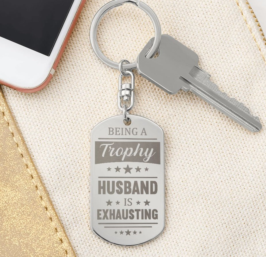 Being a trophy husband is exhausting  Create a unique keepsake with our Engraved Dog Tag Keychain. This high-quality stainless steel piece can be customized on the back in a scripted font, with 2 lines of text, up to 20 characters each.