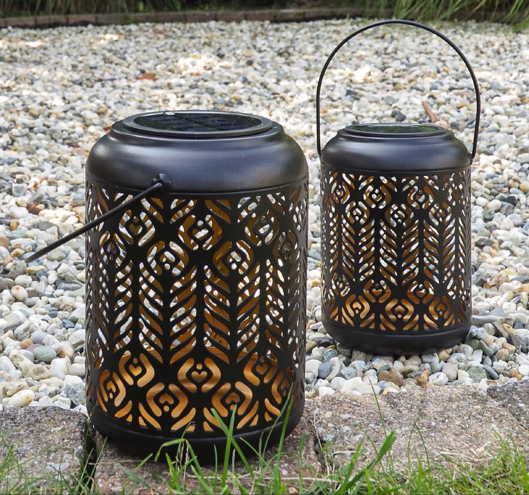 Two decorative lanterns on a pebbled surface with greenery in the background