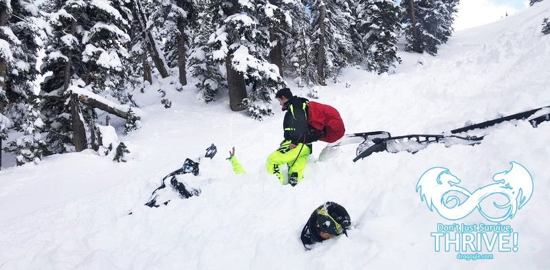 Two people in avalanche safety gear with a backpack, skiing down a snowy mountain slope.